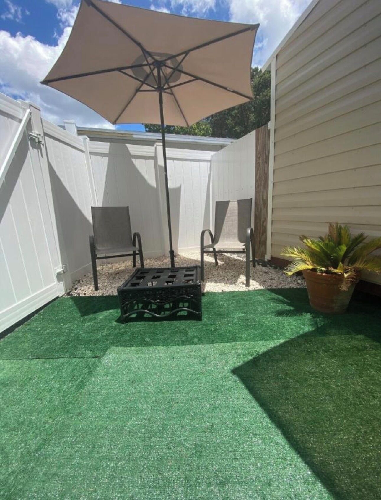 A patio with artificial grass, a table and chairs, a large umbrella, and a potted plant.