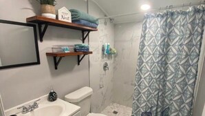 Et badeværelse med bruser, toilet, håndvask og et håndklædestativ med sammenfoldede håndklæder.