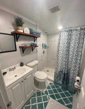 Un baño con ducha, inodoro, lavabo y un perchero con toallas dobladas.