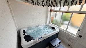 Ein Whirlpool in einem Raum mit weißen Backsteinwänden, einem Fenster und einer kleinen Holzstufe als Zugang.