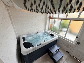 A hot tub in a room with white brick walls, a window, and a small wooden step leading to it.