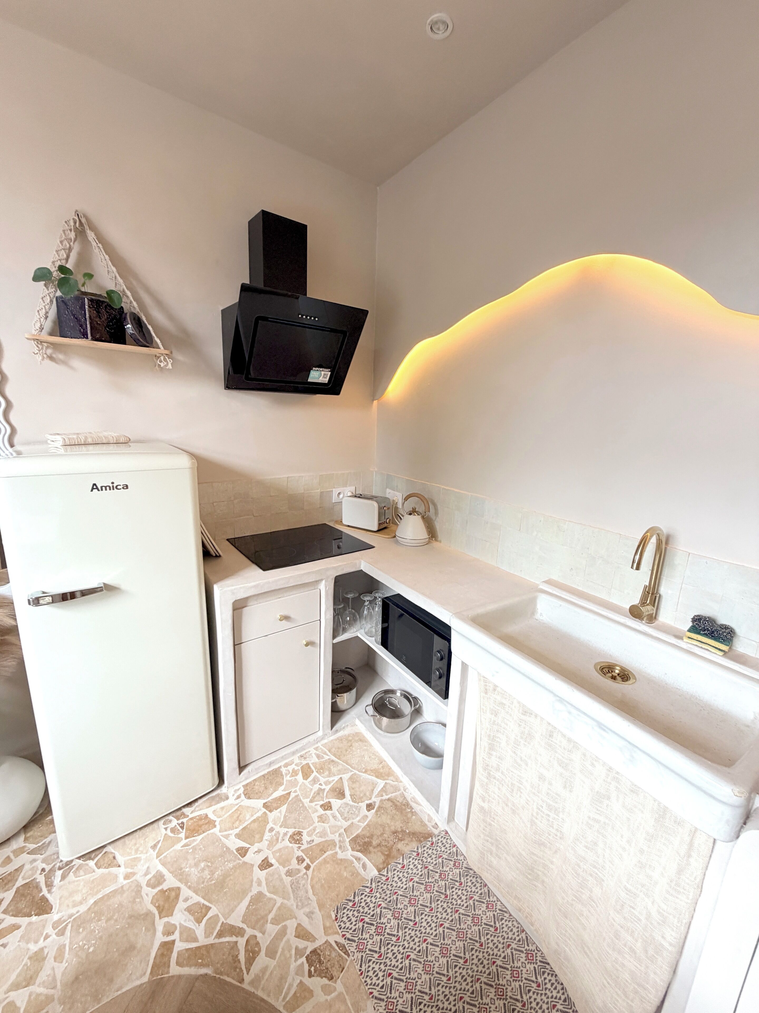 Een kleine keuken met een witte koelkast, een magnetron en een gootsteen met een gouden kraan.