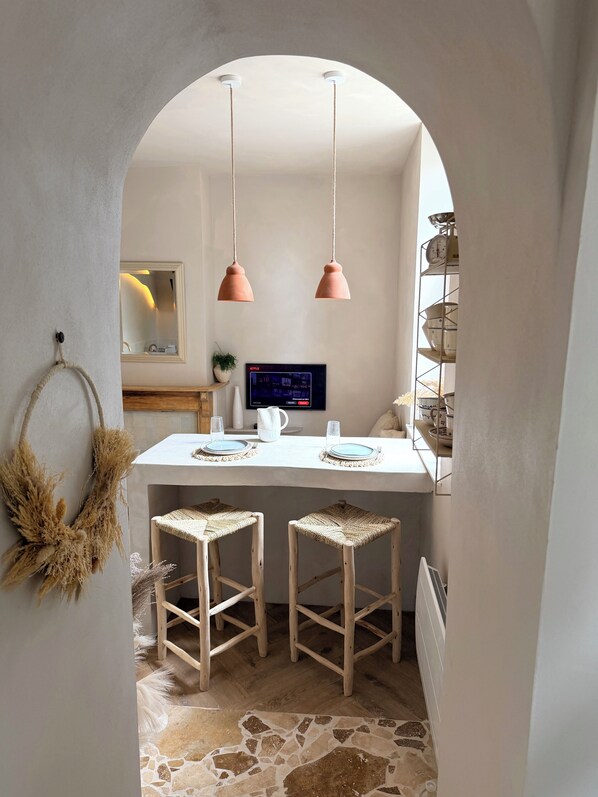 A kitchen with a white countertop, two hanging pendant lights, a television, and a shelf with kitchenware.