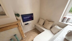 Ein modernes Wohnzimmer mit Kamin, einem wandmontierten Flachbildfernseher, einer gemütlichen Sitzecke mit Kissen und einem Fenster mit dekorativen Vasen.
