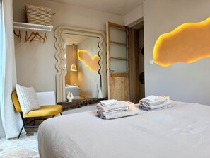 A bedroom with a bed, a chair, a mirror, and a door.