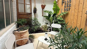 Un patio con sillas de metal blanco y una mesa, rodeado de plantas en macetas y una valla de madera.