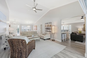 A spacious living room with a high ceiling, a ceiling fan, and a large window providing natural light. - BRAND NEW Saltwater POOL w/Spa. Waterfalls. Totally Renovated Exceptional OASIS! (Naples)