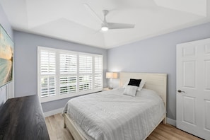 Ein Schlafzimmer mit einem Bett, einem Nachttisch, einer Lampe, einem Deckenventilator und einer Tür.