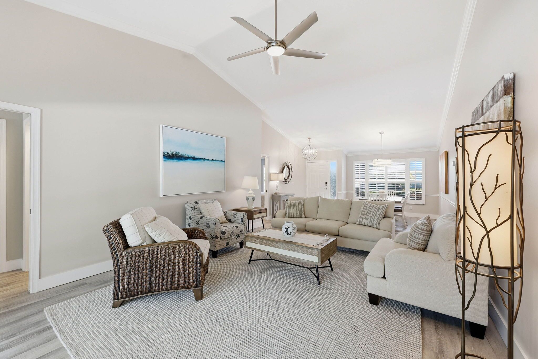 A spacious living room with a ceiling fan, a large window with blinds, and a decorative floor lamp.