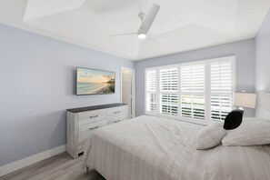 Ein Schlafzimmer mit Bett, Kommode, Deckenventilator und Fenster mit Jalousien.