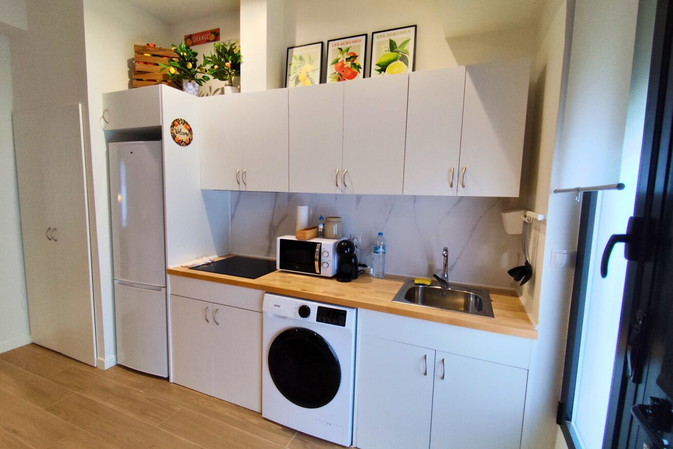 Een praktische keuken met witte kastjes, een wasmachine, een magnetron en een spoelbak.