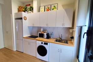 A compact kitchen with white cabinets, a washing machine, a microwave, and a sink. - Travel Habitat Loft Parque de Cabecera 1 (Valencia)