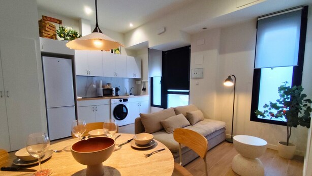 A modern kitchen with a dining area, a washing machine, and a large window.