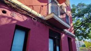 A building with a pink facade, a balcony with a black railing, and a window with a closed shutter.