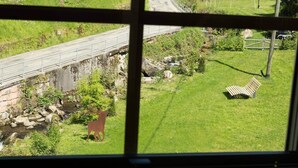 A view through a window of a grassy area with a bench, a small stream, and a bridge. - Black Forest Chalet - Wilde Rench - "Red Kite" (Bad Peterstal-Griesbach)
