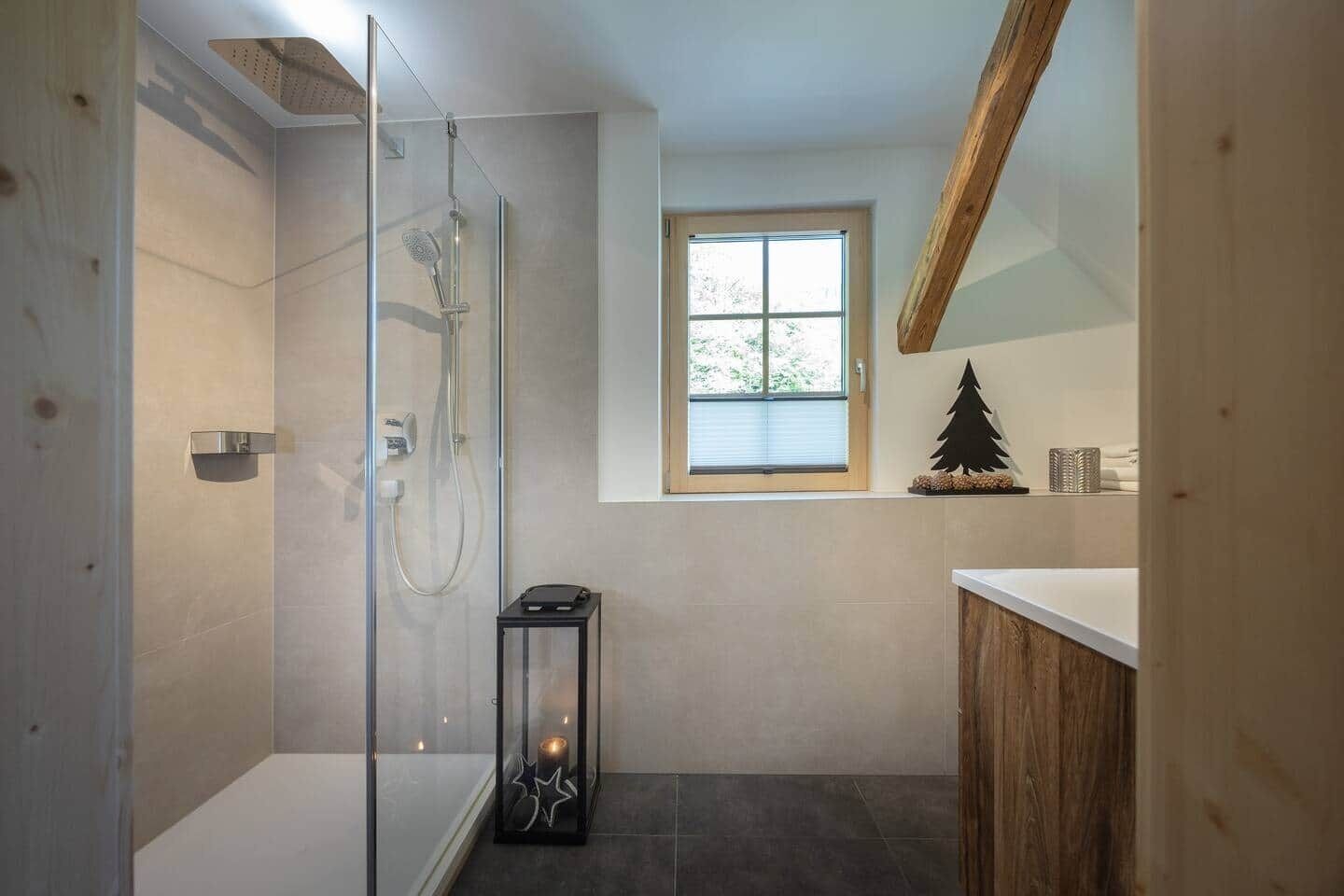 A modern bathroom with a glass-enclosed shower, a small window, and a wooden vanity.