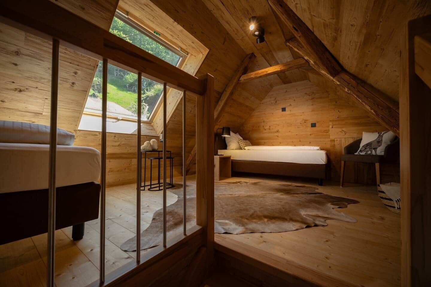 Ein gemütliches Schlafzimmer im Dachgeschoss mit schrägen Wänden, einem Bett, einem Sessel und einem kleinen Tisch.