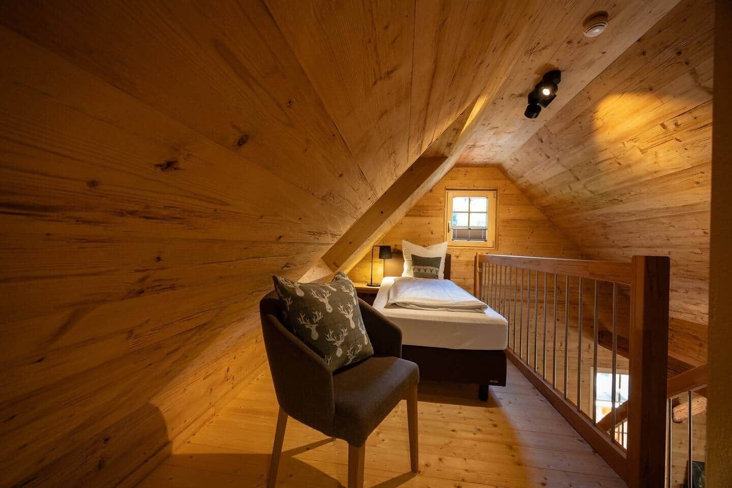 A cozy attic bedroom with a bed, a chair, and a window.