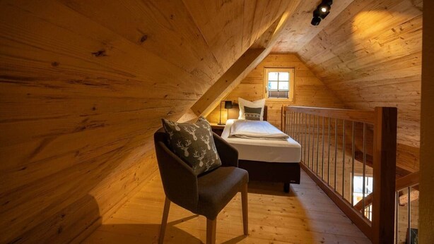 Une chambre mansardée chaleureuse, avec un lit, une chaise et une fenêtre.