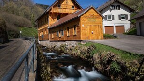 Un bâtiment en bois doté d’un balcon, une enseigne indiquant « SCHWARZWALD CHALET », et un ruisseau en contrebas.