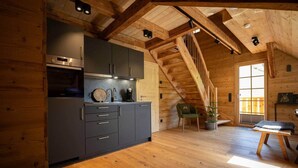 Une cuisine moderne avec des meubles de couleur sombre, un four encastré et un escalier en bois menant à une mezzanine.