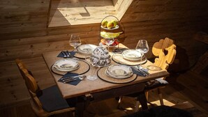 Une table à manger dressée avec des assiettes, des couverts et des verres, agrémentée d’un panier de fruits et d’un objet décoratif.