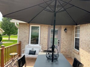 Een terras buiten met een tafel, stoelen en een grote parasol.