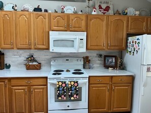 Una cocina con armarios de madera, un microondas blanco, una estufa y un refrigerador.
