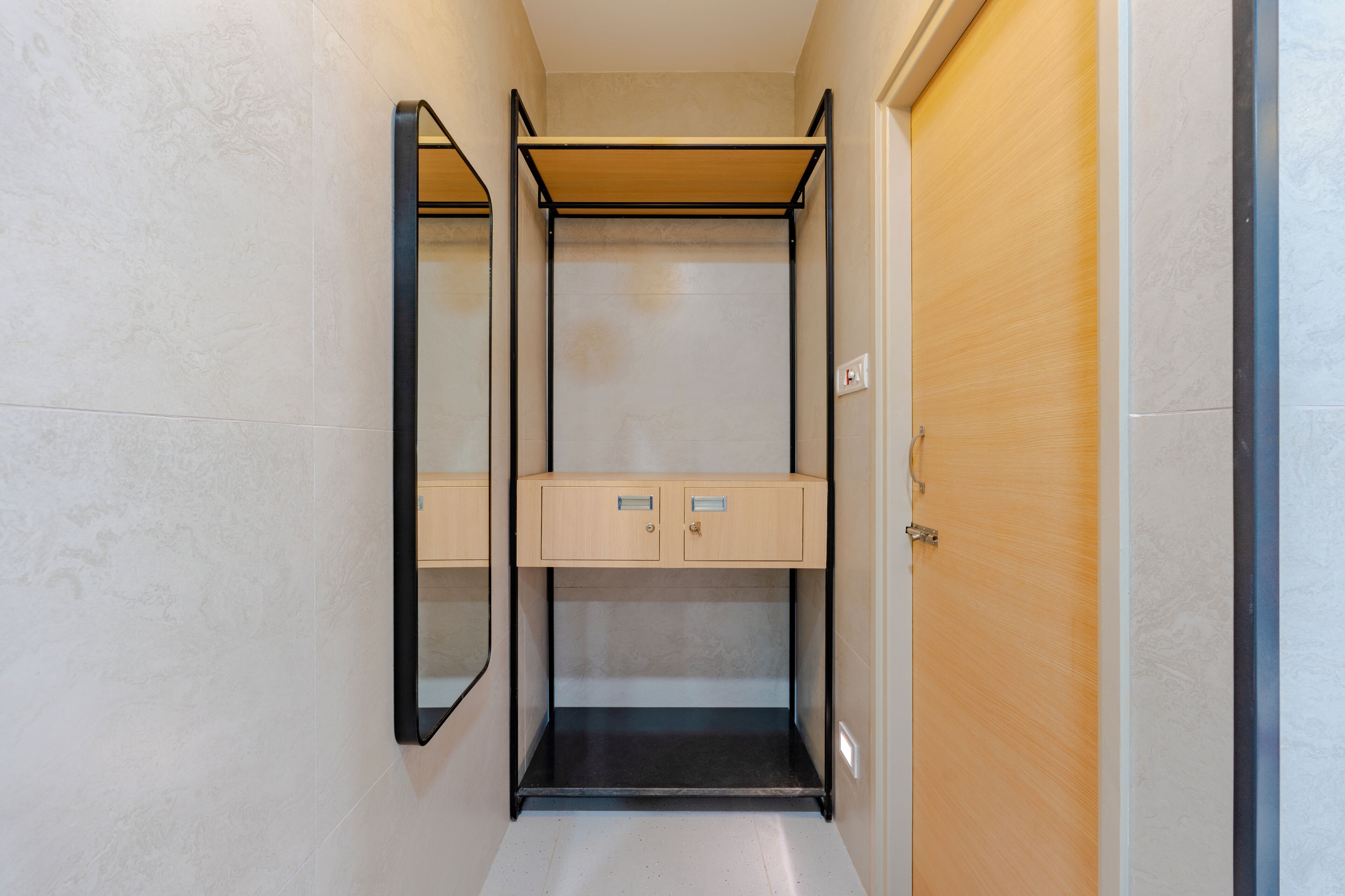 A narrow hallway with a wooden door on the right and a mirrored closet with a shelf unit in the center.