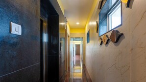 Un pasillo con piso de mármol, una puerta a la izquierda y un muro con un aplique y un espejo.