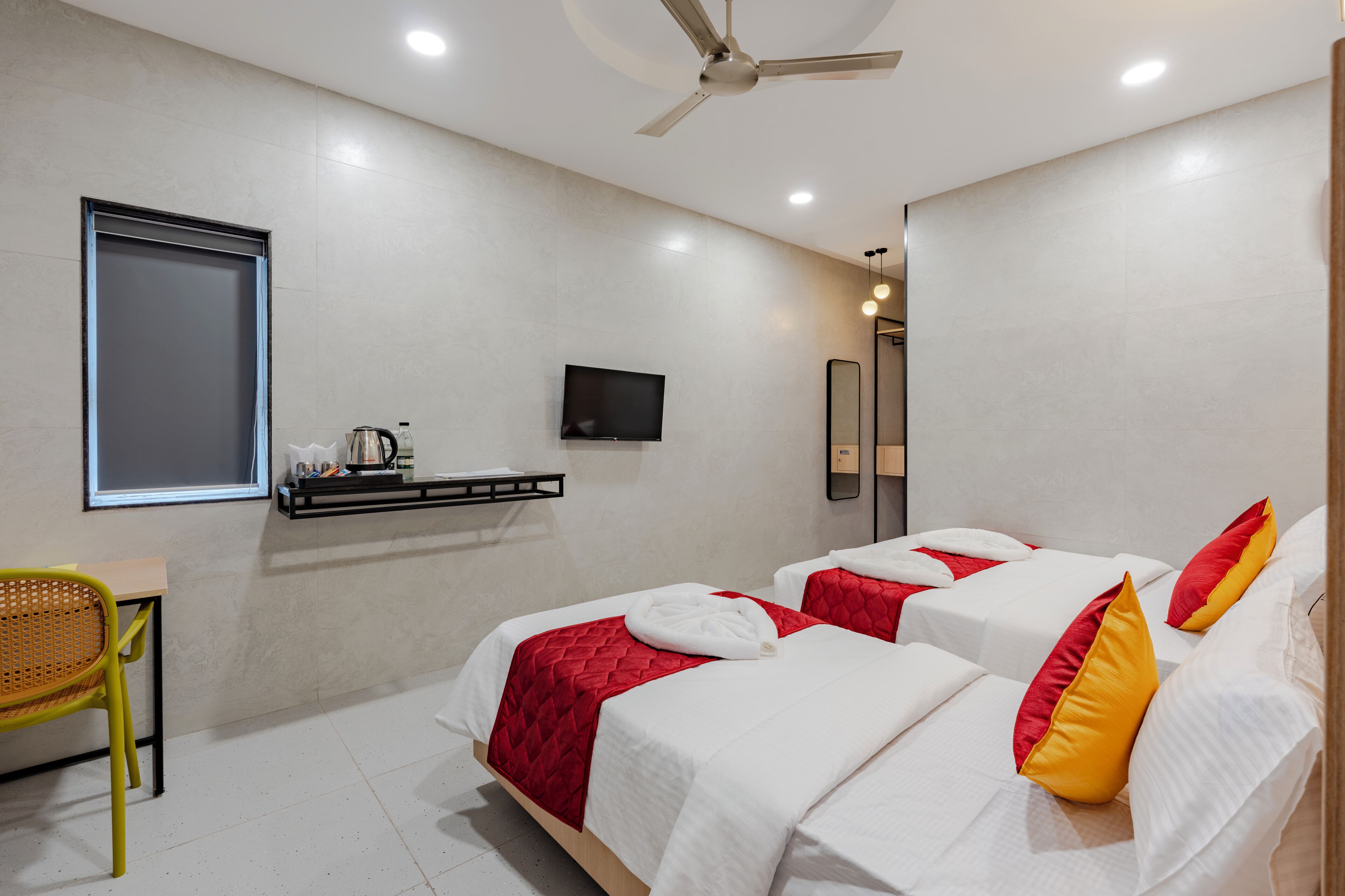 A hotel room with two beds, a TV, a desk, and a chair.