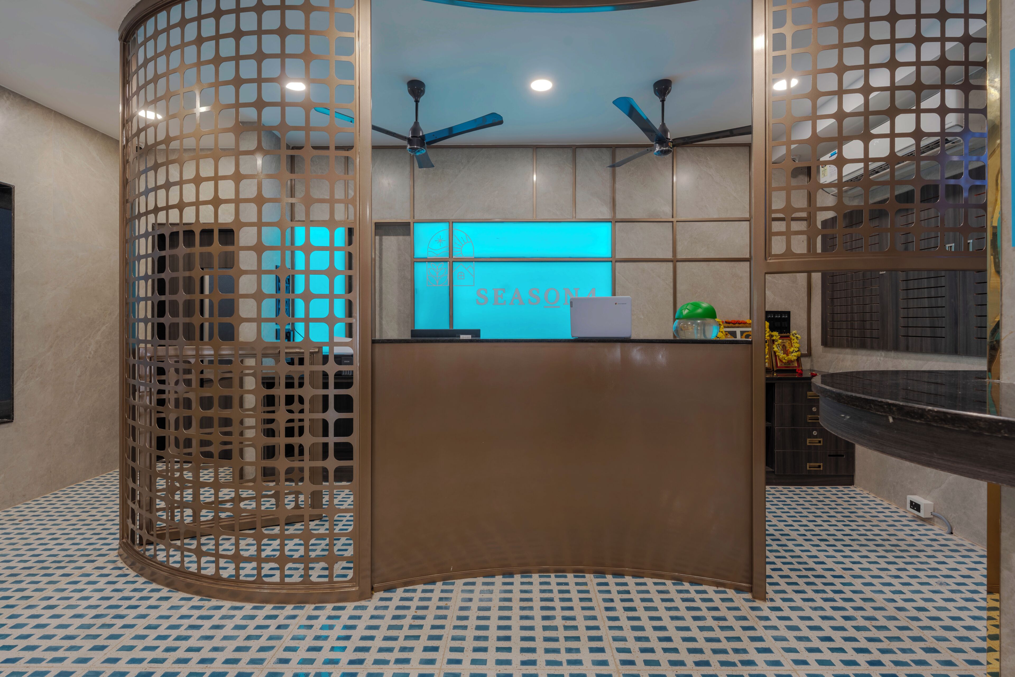 Una zona de recepción con diseño moderno, que presenta un mostrador curvo, un letrero iluminado en azul y ventiladores de techo.