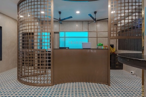 Una zona de recepción con diseño moderno, que presenta un mostrador curvo, un letrero iluminado en azul y ventiladores de techo.