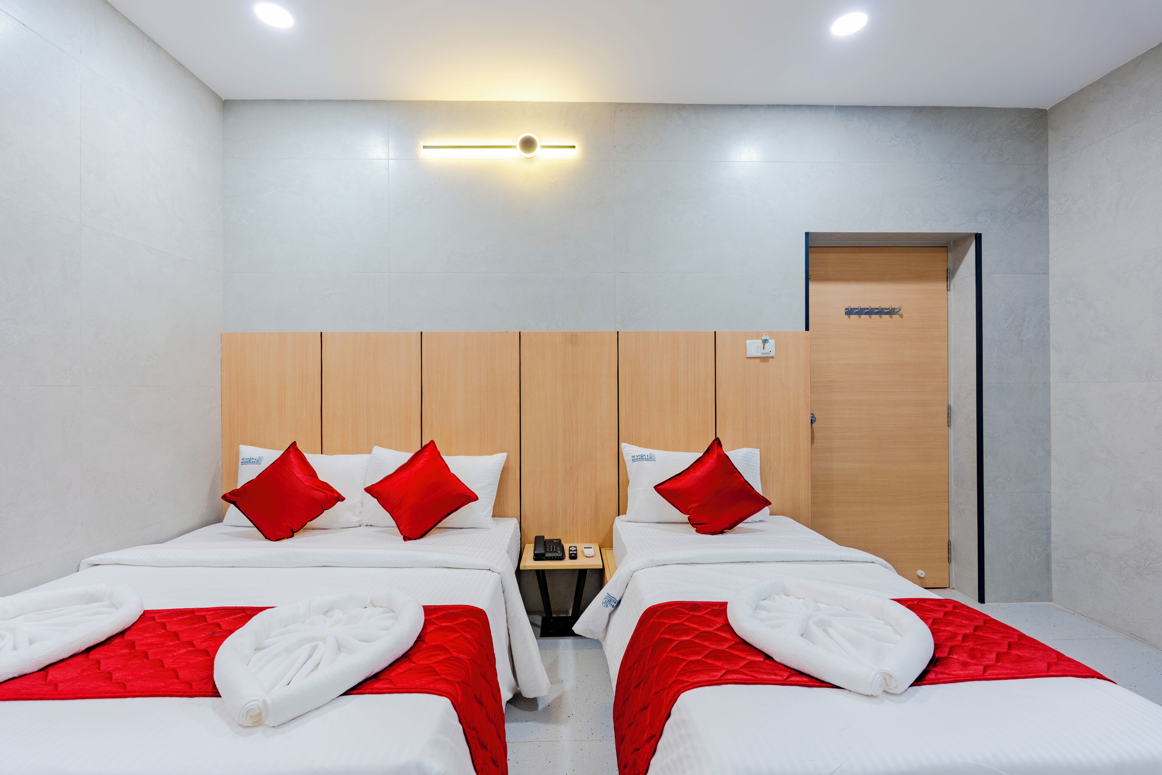 Habitación de hotel con dos camas, cada una con ropa de cama roja y blanca, cabecero de madera y una mesita de noche pequeña con un teléfono y un control remoto.