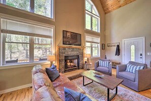 Ein geräumiges Wohnzimmer mit Kamin aus Stein, Ledersofas und großen Fenstern.