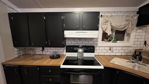 Una cocina con gabinetes negros, una estufa blanca y un ventanal con cortina.