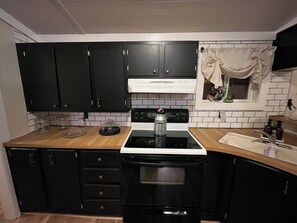 Een keuken met zwarte kastjes, een witte kookplaat en een raam met gordijn.