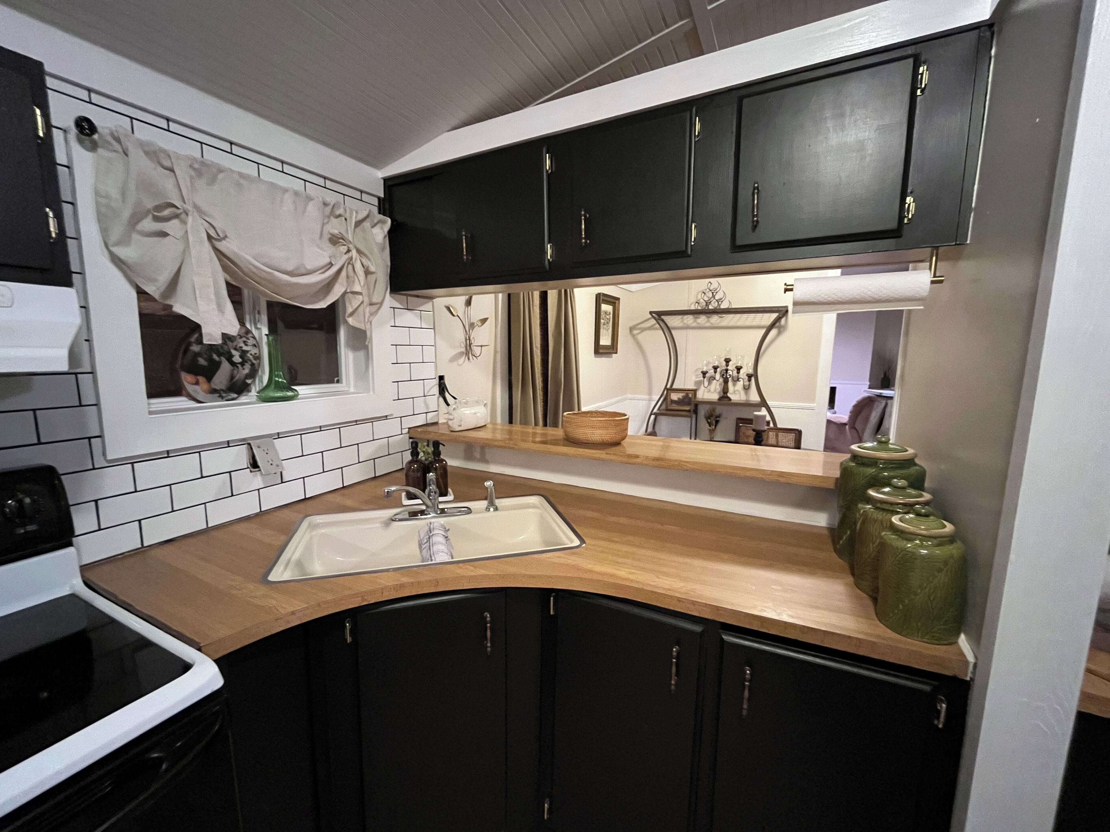Una cocina con gabinetes negros, un lavamanos blanco y una ventana con cortina.