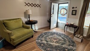 Una sala de estar con un sofá verde, un tapete redondo, piso de madera, una lámpara y una puerta que da al exterior.