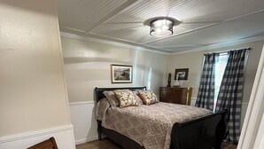 Un dormitorio con una cama, una silla de madera, un aparador y un cuadro en la pared.