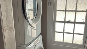 Ein Waschraum mit vertikal gestapelter Waschmaschine und Trockner, einem Fenster mit Milchglas und einem Schild über dem Fenster mit der Aufschrift 'Laundry Room'.