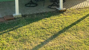 Ein überdachter Patio-Bereich mit Tisch, Stühlen, einem Mülleimer und einem Gartenschlauch.