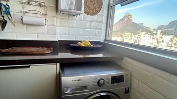 Uma cozinha compacta com máquina de lavar, janela e vista para a cidade, e prateleira com utensílios de cozinha.