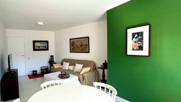 Uma sala de estar com uma parede verde de destaque, um sofá branco, uma mesa de jantar com cadeiras e obras de arte emolduradas nas paredes.
