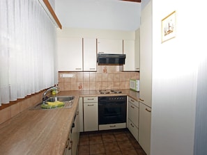 A compact kitchen with a sink, stove, oven, and microwave. - Cadras 23 Appartement/Fewo, Bad, WC, 1 Schlafraum 2 Zimmerwohnung - 4 Betten by Interhome (Tinizong)