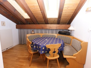 A dining area with a round table covered by a blue tablecloth with a leaf pattern, surrounded by wooden chairs with cushioned seats. - Cadras 23 Appartement/Fewo, Bad, WC, 1 Schlafraum 2 Zimmerwohnung - 4 Betten by Interhome (Tinizong)