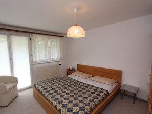 Ein Schlafzimmer mit einem Bett, einem Sessel, einem Nachttisch, einem Heizkörper und einem Fenster mit Vorhängen.