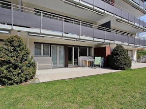 Ein modernes, zweistöckiges Wohnhaus mit Balkon, einer kleinen Sitzgelegenheit im Freien und einem gepflegten Rasen.