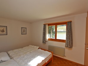A bedroom with a wooden bed, a window with curtains, and two framed pictures on the wall. - Alexandra Appartement/Fewo, Bad, WC, 3 Schlafräume 4.5 Zimmerwohnung - 6 Betten by Interhome (Tinizong)