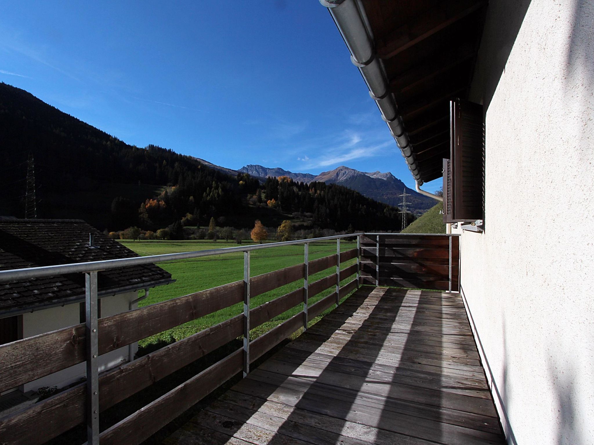 A balcony with a view of a green field and mountains.